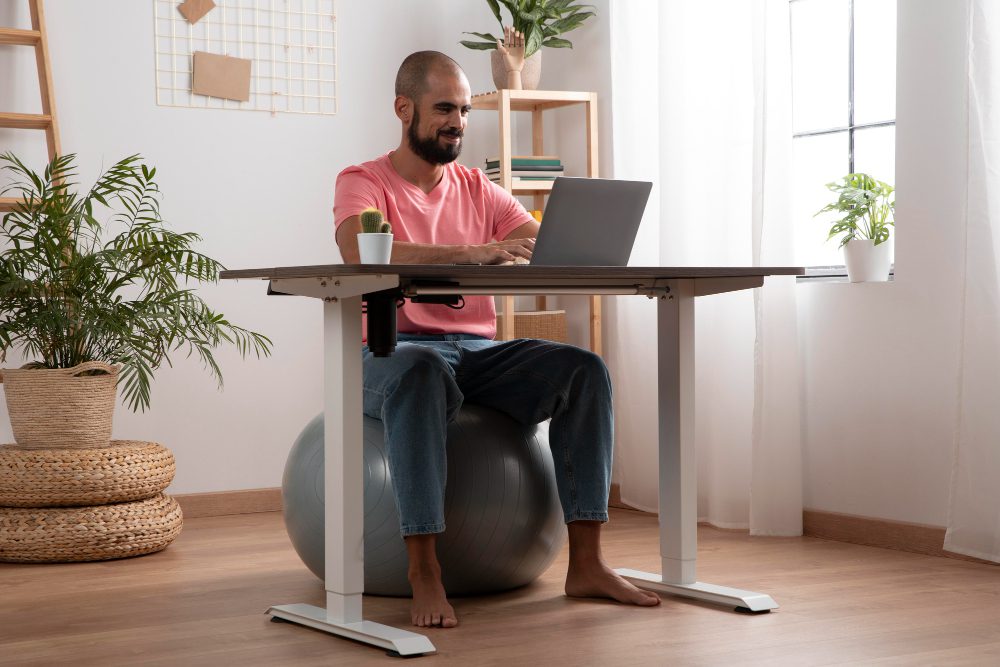 A man sits on an exercise ball at a standing desk.