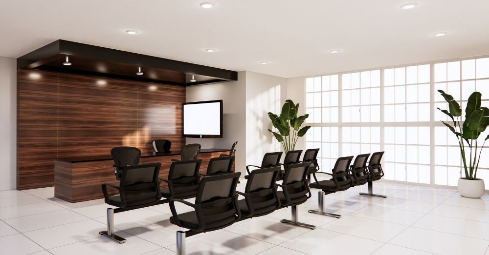 A modern waiting area with rows of black chairs facing a large wooden reception desk.