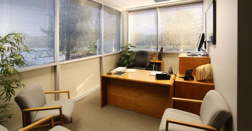 An empty office space featuring a large wooden desk with a black rolling chair behind it.