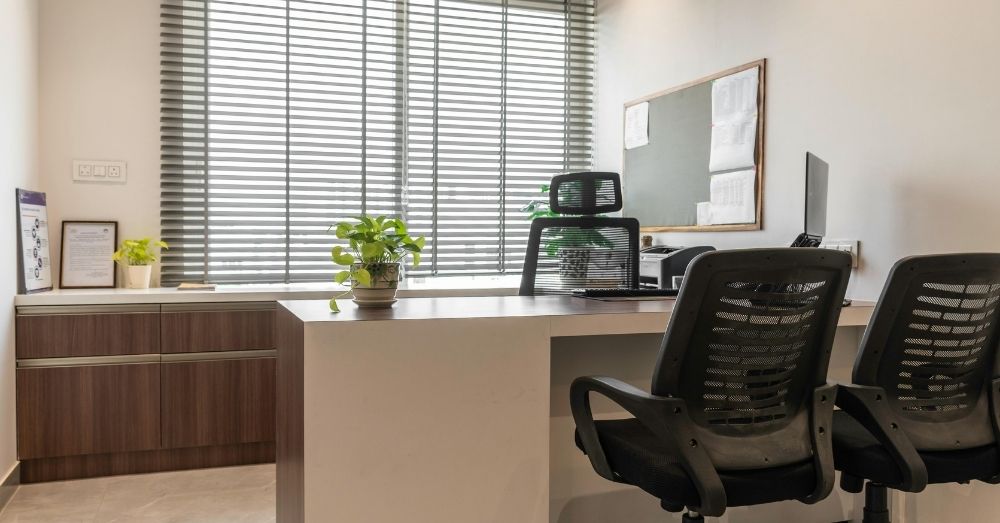 A modern office with two mesh chairs and blinds, potentially Herman Miller.