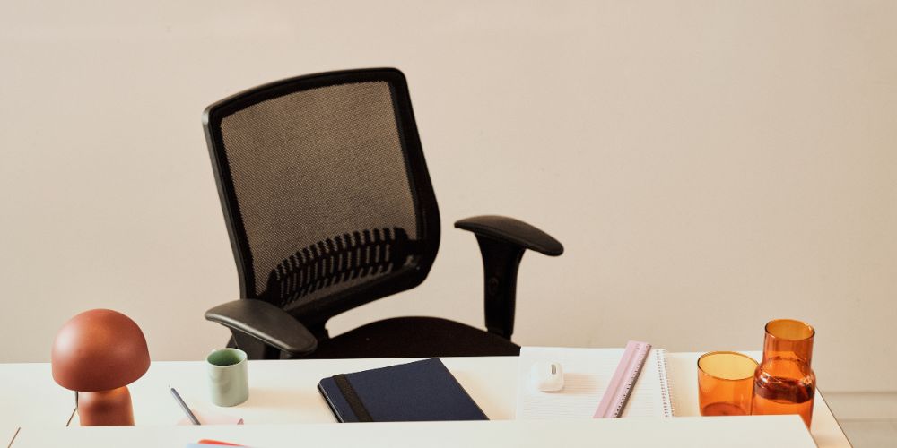 A close-up of a white desk setup featuring a black mesh ergonomic office chair
